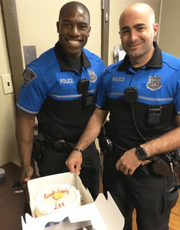 Two police officers posing next to a cake that says "Good luck, Lee!"