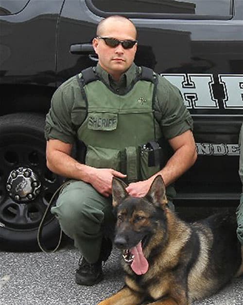 A police officer kneeling next to a squad car with his K9